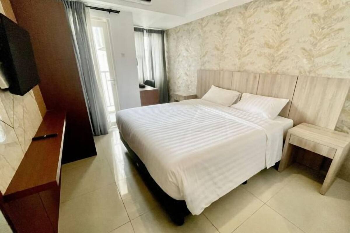 A hotel room with a large bed, a wooden headboard, a nightstand, and a desk with a chair.