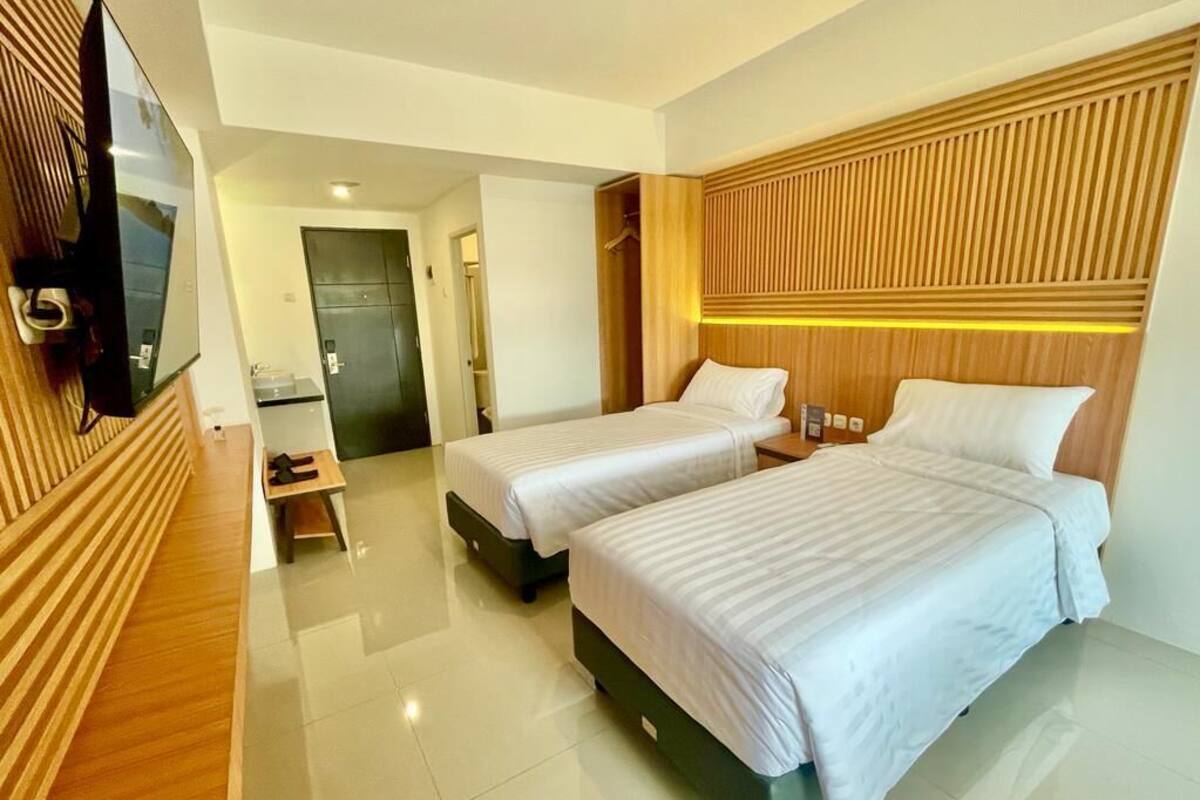 A hotel room with two beds, a TV mounted on the wall, and a wooden panel design on the headboard.