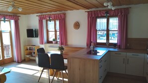 A cozy kitchen with wooden cabinets, a central island, and pink curtains. - Ferienwohnung Zuhaus, 76m², 2 Schlafzimmer, Balkon, TV, 4 Sterne, 4 Pers (Anger)