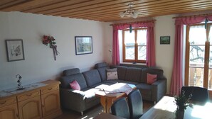 A cozy living room with a sofa, a dining table, and a wooden cabinet. - Ferienwohnung Zuhaus, 76m², 2 Schlafzimmer, Balkon, TV, 4 Sterne, 4 Pers (Anger)