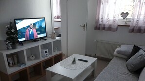 A living room with a television on a white stand, a white coffee table with a remote control, a grey sofa, and a small plant on the table. - Apartment Amina by Interhome (Braunlage)