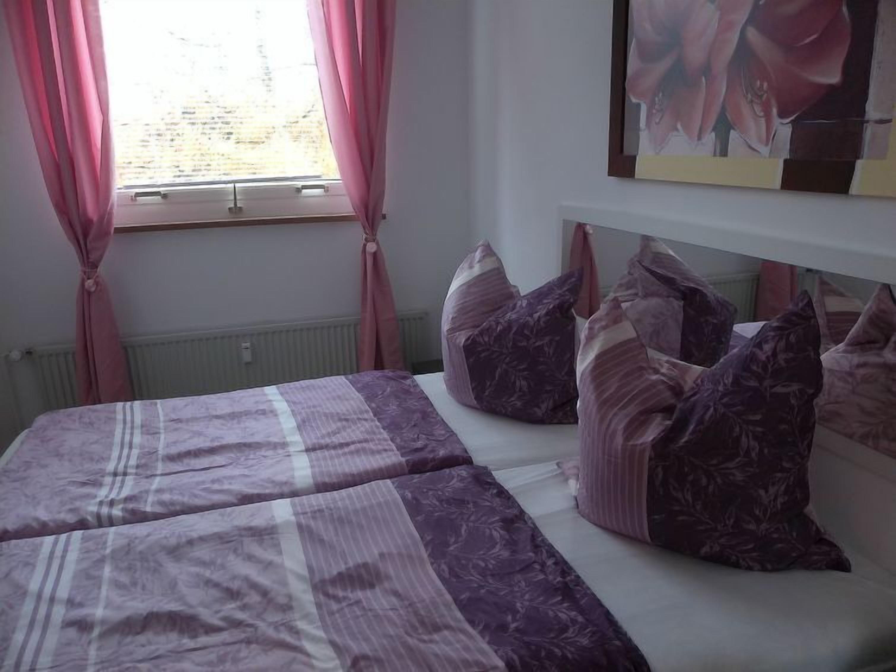 A bedroom with a bed, pillows, a window with curtains, and a wall-mounted picture.