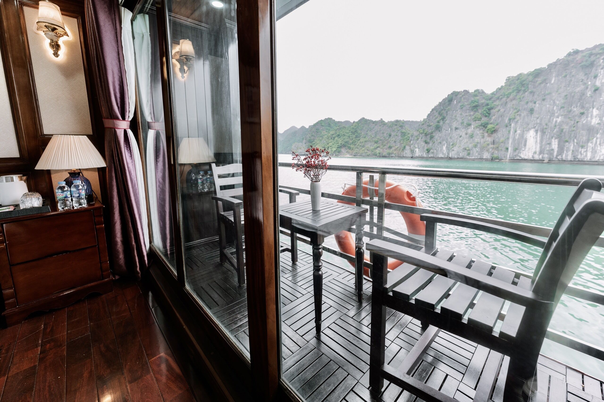 A wooden deck with a table and chairs, a wooden dresser, and a window with curtains.