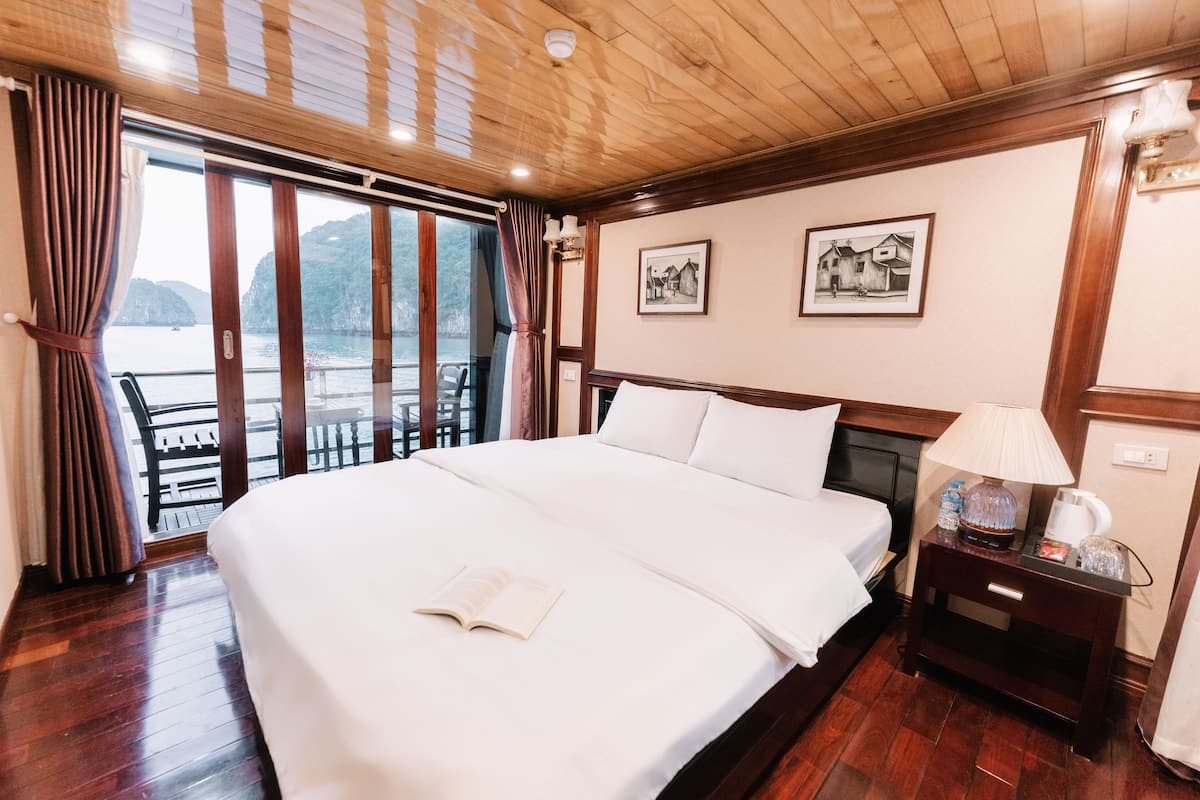 Habitación de hotel con una cama grande, una mesita de noche con lámpara, un cuadro en la pared y vista al mar por la ventana.