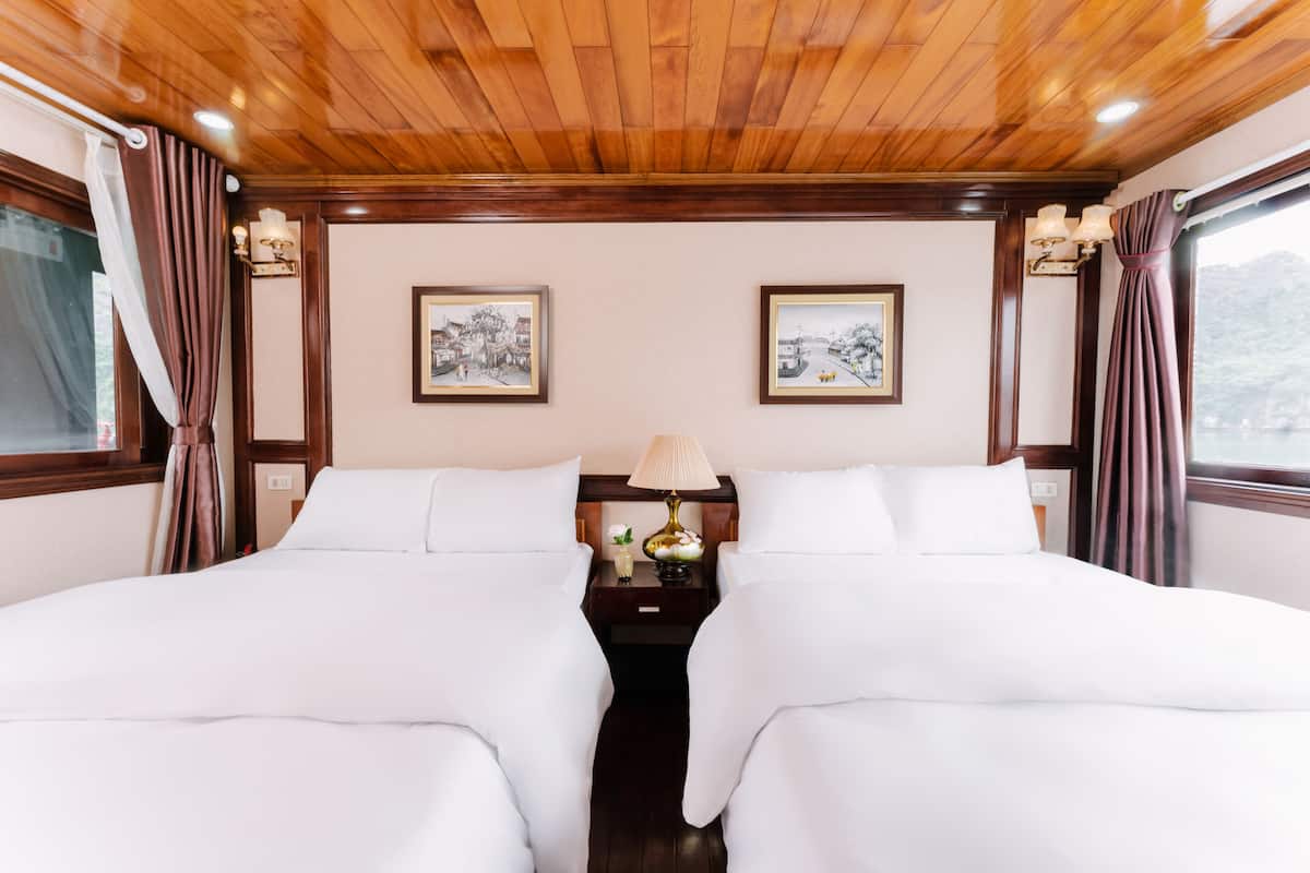 Una cama doble con ropa de cama blanca, una mesita de noche con lámpara y dos cuadros en la pared.