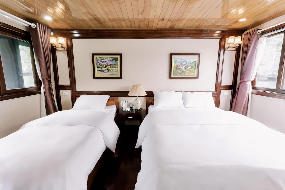 Habitación de hotel con dos camas, techo de madera, lámparas fijadas a la pared y cuadros enmarcados.