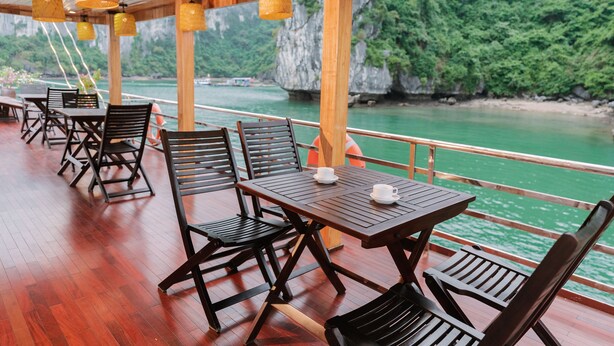 Een houten terras met tafels en stoelen met uitzicht op een rivier.