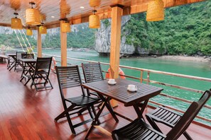 Une terrasse en bois, avec des tables et des chaises, donnant sur une rivière.