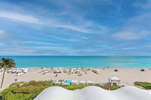 A beach with sun loungers and umbrellas, a pool, and a view of the ocean. - New! Modern Beach Resort - Ocean View & Access (Sunny Isles Beach)