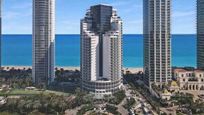 A high-rise hotel with a curved facade, located near a beach with palm trees and a clear blue sky. - New! Modern Beach Resort - Ocean View & Access (Sunny Isles Beach)