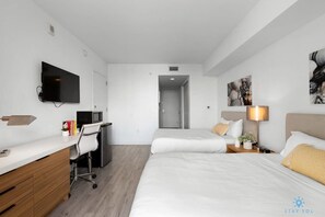 A modern hotel room with two beds, a desk with a chair, a flat-screen TV, and artwork on the walls.
