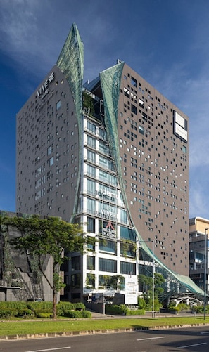 A modern hotel with a unique curved glass facade, multiple floors, and a prominent entrance with a sign. - VIVERE Hotel, ARTOTEL Curated (Gading Serpong)