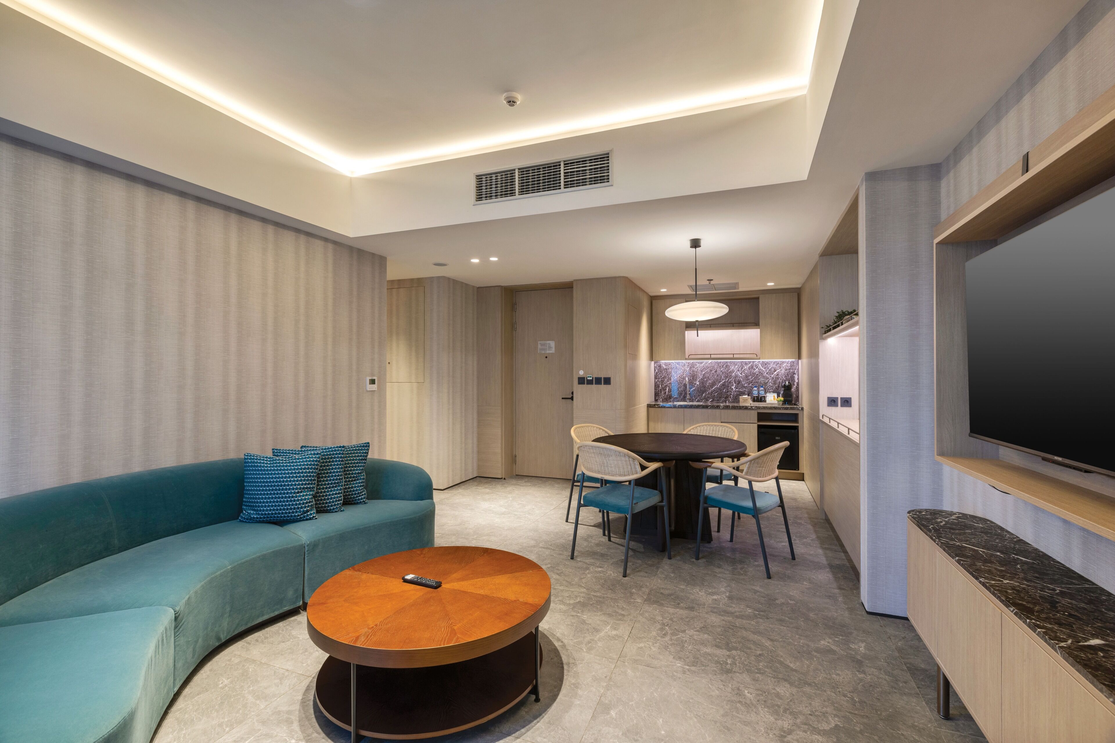 A modern living room with a sofa, a round coffee table, a dining table with chairs, a TV, and a kitchen area.