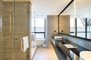 Un baño moderno con ducha envuelta en vidrio, bañera independiente, un espejo grande y encimera oscura con lavabo y tocador.