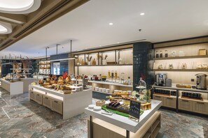 Un moderno vestíbulo de hotel con suelo de mármol, una recepción central y diversas comodidades, como una estación de café y objetos decorativos.