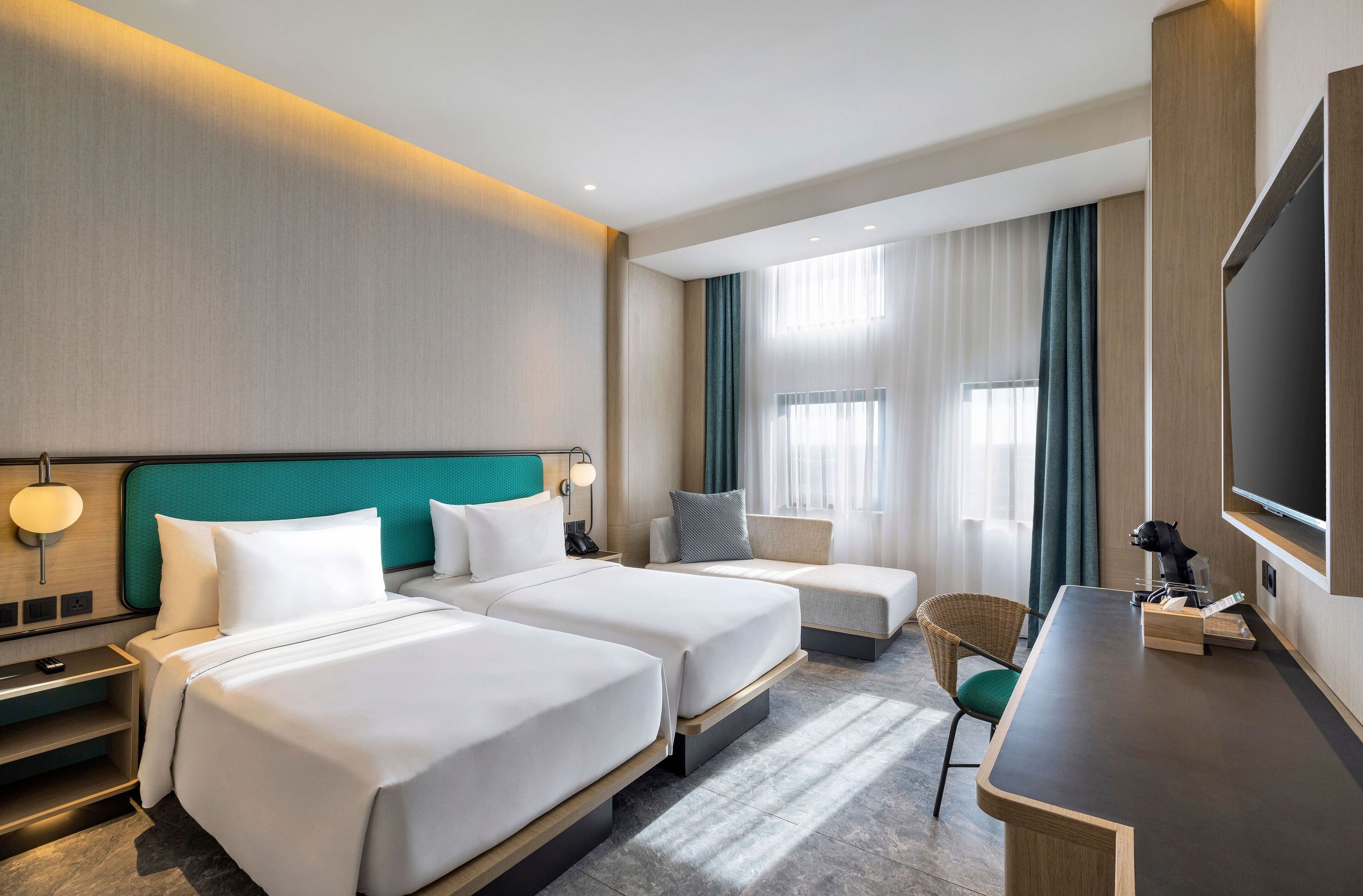 Habitación de hotel con dos camas, un escritorio, una silla, un televisor y una ventana con cortinas.