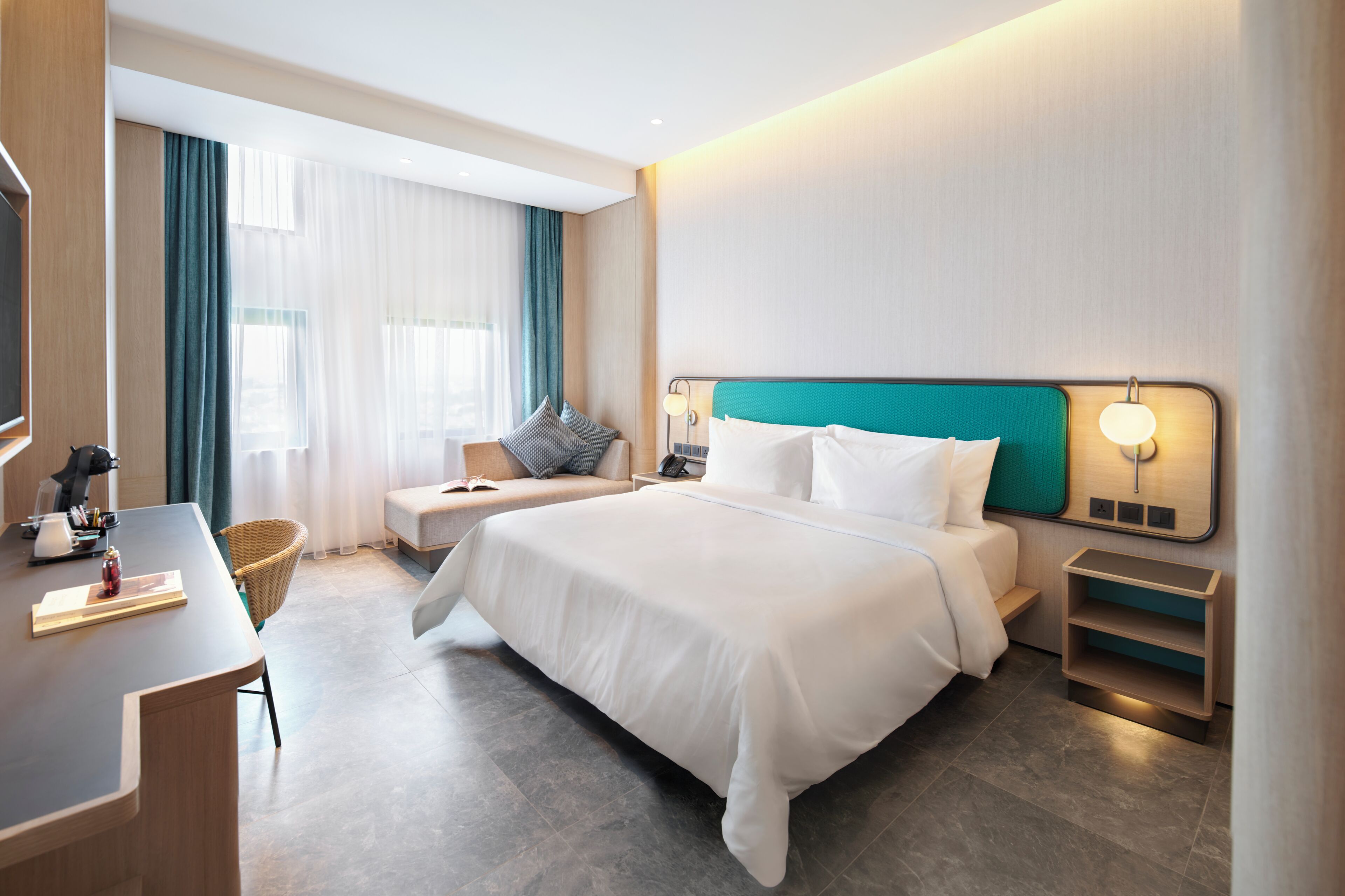 Une chambre d’hôtel avec un lit, des tables de chevet, un bureau, une chaise et une fenêtre avec des rideaux.
