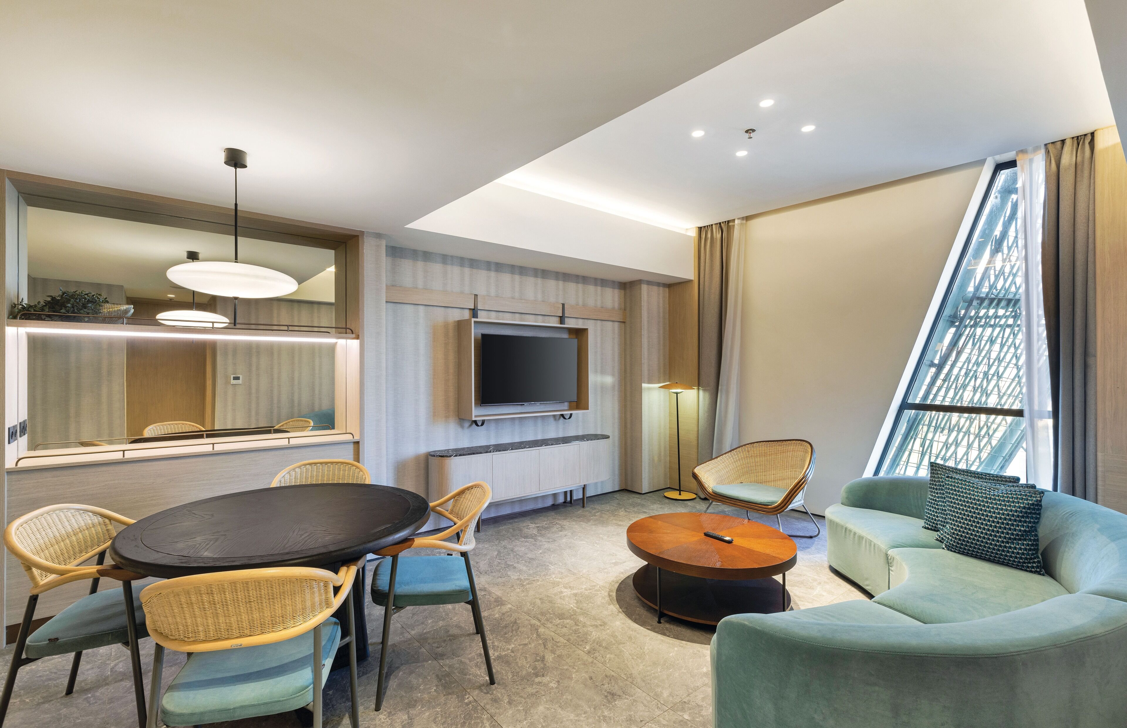 A modern hotel room with a dining area, a sofa, a TV, and a large window.