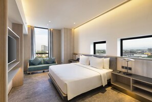 Habitación de hotel moderna con una cama grande, un sofá, un televisor y vistas a la ciudad.