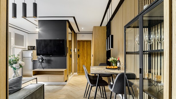 A modern kitchen with a TV, wooden cabinets, and a dining area with a table and chairs. - Mokotów Sobieskiego (Warsaw)