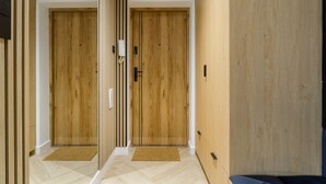 A hallway with two wooden doors, a doormat, and a light switch on the wall. - Mokotów Sobieskiego (Warsaw)