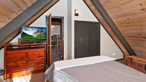 Un dormitorio con cama, cómoda y televisor en una habitación con techo inclinado.