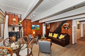 Un salon chaleureux avec une cheminée, des murs en bois, un canapé en cuir et une table à manger avec des chaises.