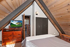 Ein Schlafzimmer mit schrägem Dach, einer Holzkommode, einem Bett und einem Fernseher.