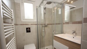 Une salle de bain moderne avec une douche à parois de verre, des toilettes blanches et un lavabo avec un meuble-vasque en bois.