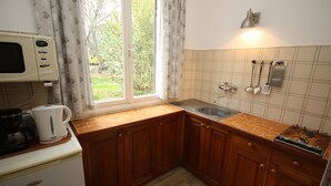 Une cuisine de taille réduite, dotée de meubles de rangement en bois, d’un four à micro-ondes encastré et d’une fenêtre agrémentée de rideaux.