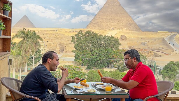 Two men dining outdoors with a view of the pyramids in the background. - Germania pyramids inn (Giza)