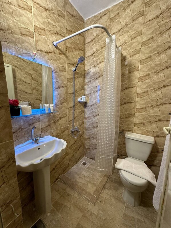 A bathroom with a shower, toilet, sink, and a mirror.