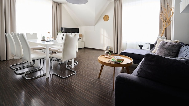 Moderni hotellihuone, jossa on ruokailutila, sohva, pyöreä puinen pöytä ja televisio.
