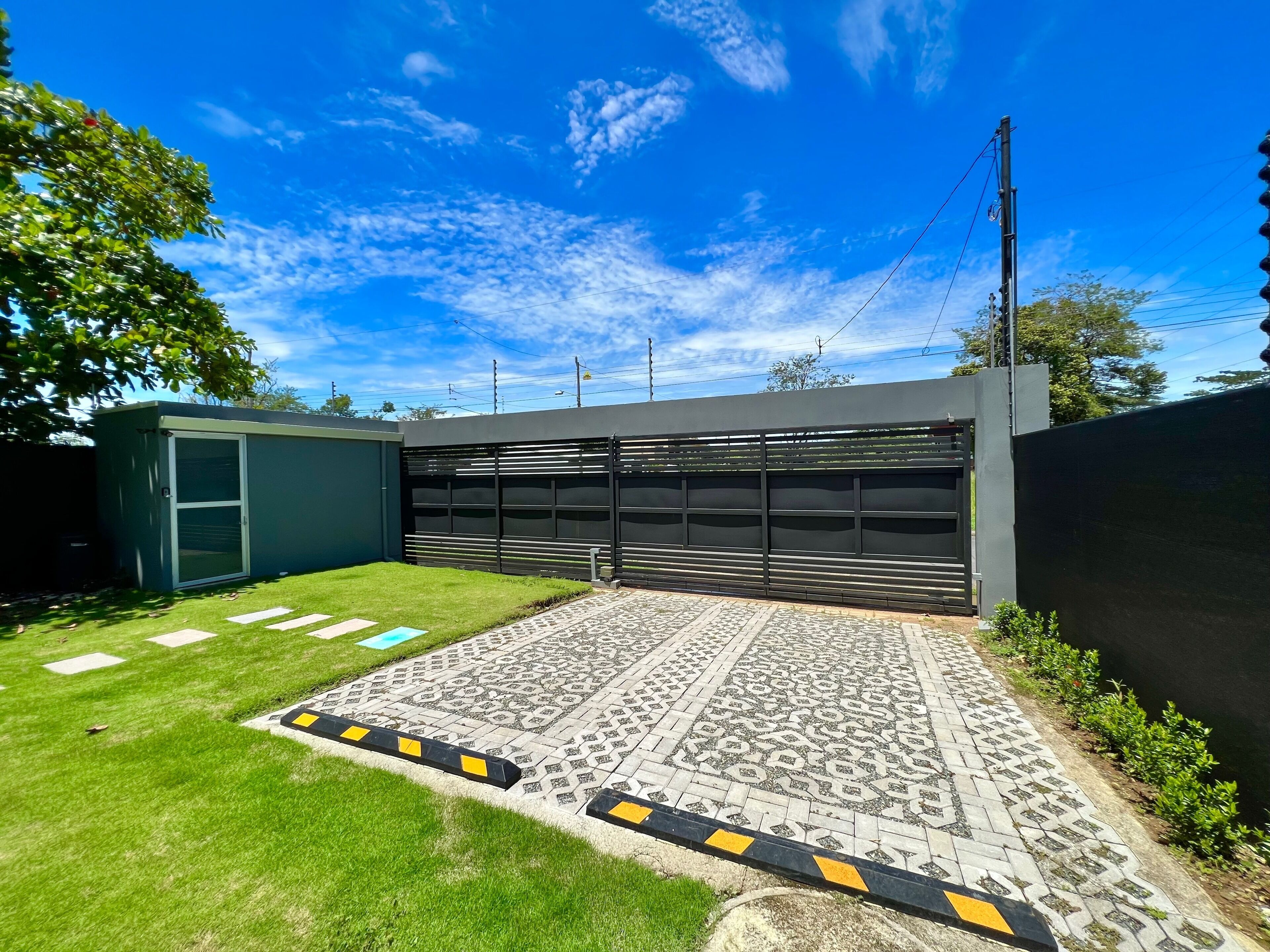 A modern garage with a large black door, a paved driveway with yellow and black curbs, and a well-maintained lawn.