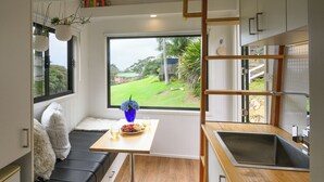 A compact kitchen with a built-in bench seating area, a large window offering a view of the outdoors, and a small dining table with a vase of flowers.