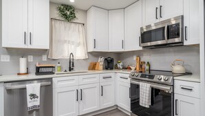 Una cocina moderna con armarios blancos, un microondas de acero inoxidable, un horno y un lavavajillas.