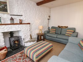 Una sala acogedora con pared de piedra, chimenea, sofá y un otomano de colores.