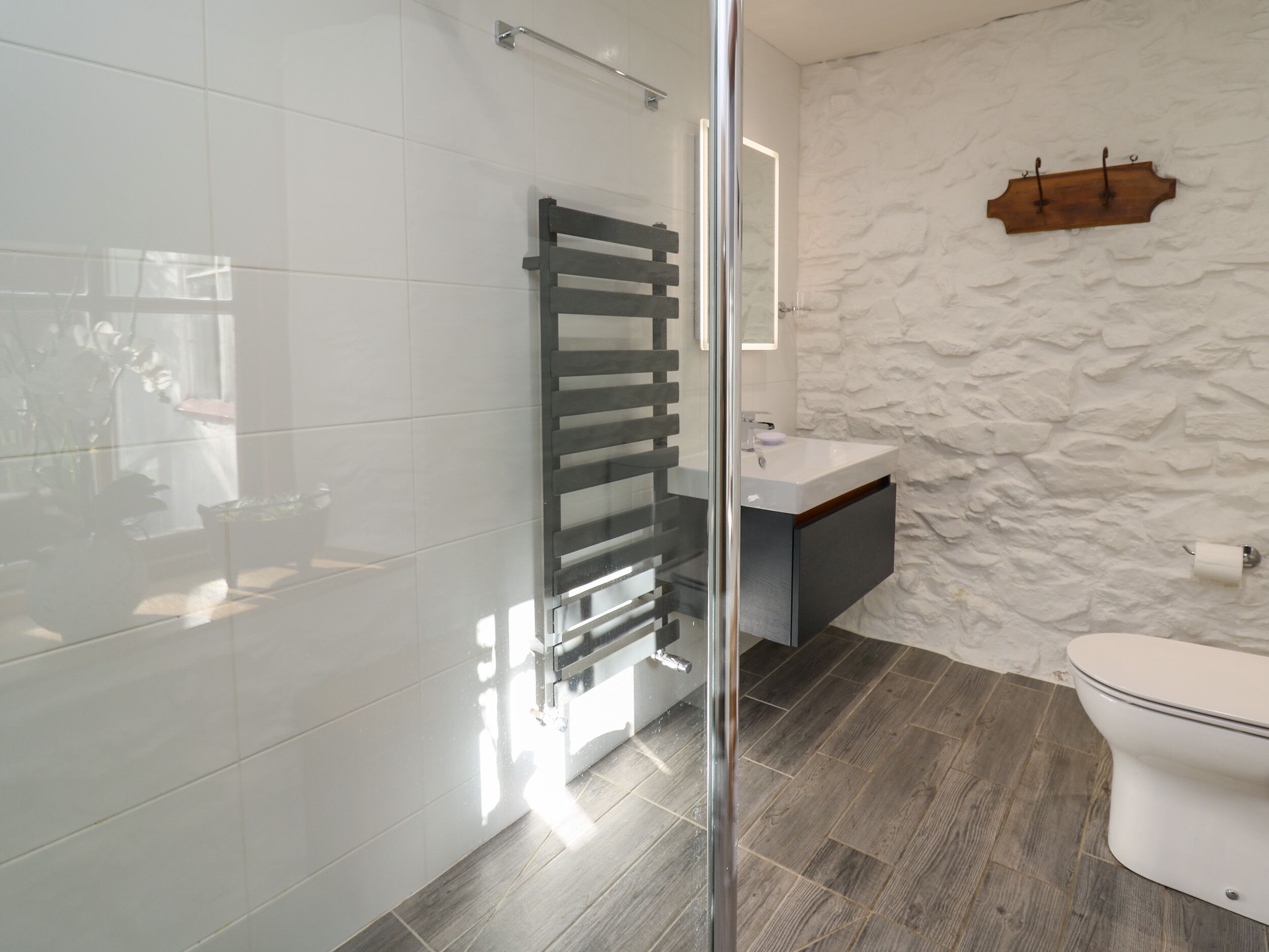 A modern bathroom with a glass shower enclosure, a white sink, and a wooden wall feature.
