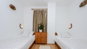 Ein Zimmer mit zwei Betten, einem hölzernen Schminktisch, einer Pflanze und einem Vorhang.