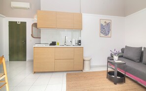 Un apartamento moderno con kitchenette, un sofá gris, una pequeña mesita auxiliar y una obra enmarcada en la pared.