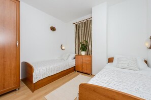 Quarto com duas camas de solteiro, um guarda-roupa de madeira, um pequeno armário, uma planta em vaso e uma cortina.