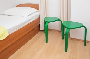 Una cama individual con cabecera de madera, almohada blanca y manta amarilla. Hay dos sillas verdes con patas curvadas.
