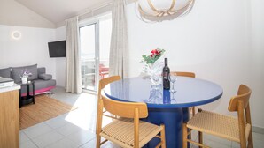 Een moderne woonkamer met een ronde eettafel, twee stoelen, een bank, een televisie en een groot raam met gordijnen.