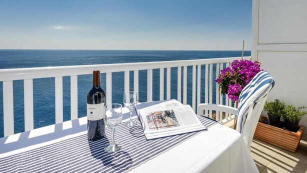 Ein Tisch ist gedeckt mit einer Weinflasche, Gläsern und einer Speisekarte auf einem Balkon mit Meerblick.