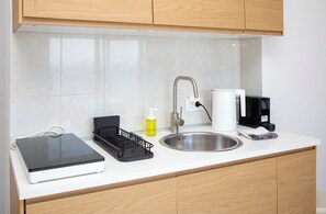 Una cocina moderna con un lavamanos de acero inoxidable, un electrodoméstico negro, un escurreplatos, una botella de detergente para trastes y una cafetera blanca.