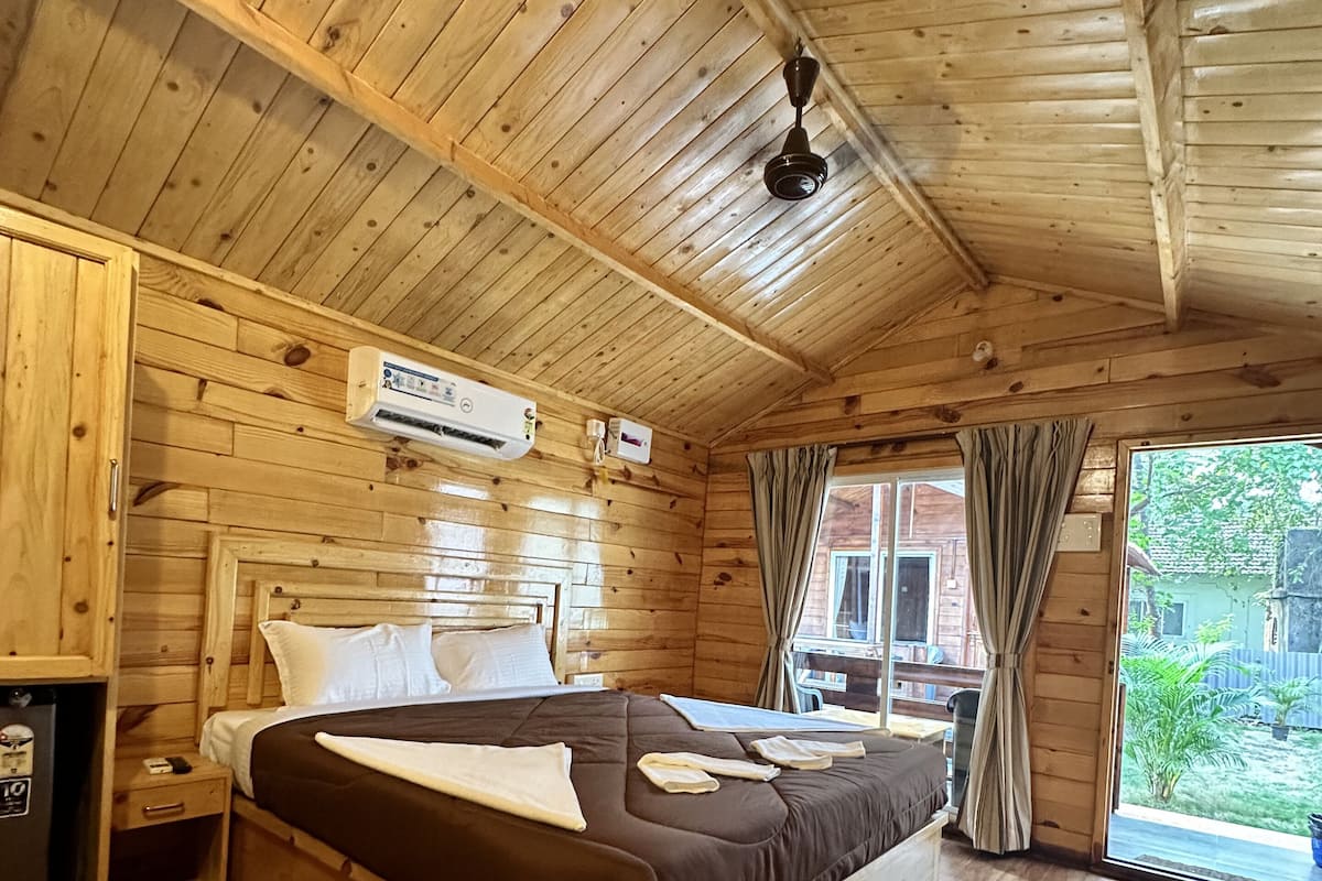 A wooden cabin bedroom with a bed, nightstand, and an air conditioning unit.