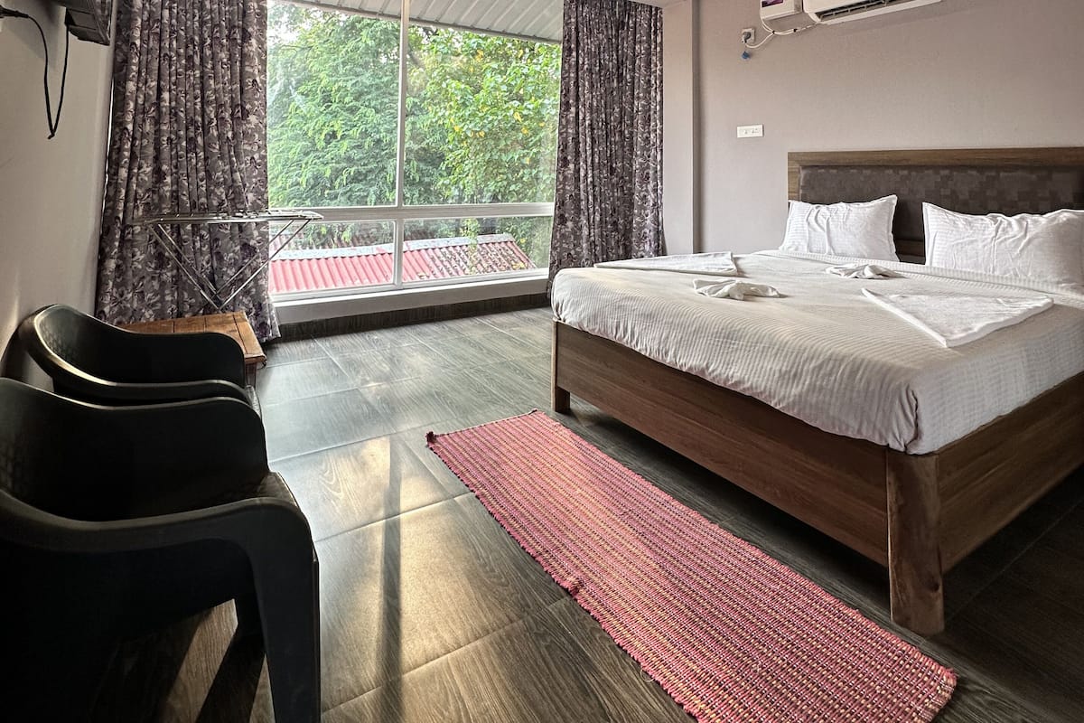A hotel room with a bed, a ceiling fan, an air conditioner, a TV mounted on the wall, and a window with curtains.