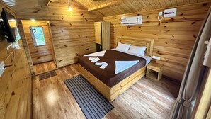 Una habitación de cabaña de madera con una cama, una mesita de noche, un calentador y una ventana.