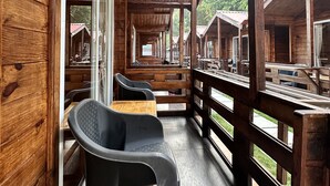 Una terraza de madera con asientos y mesas, con vistas a una hilera de cabañas.