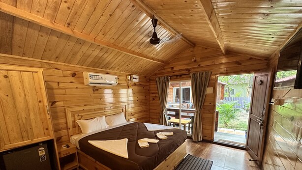 Un dormitorio de cabaña de madera con cama, un refrigerador pequeño y una puerta corrediza de vidrio al exterior.